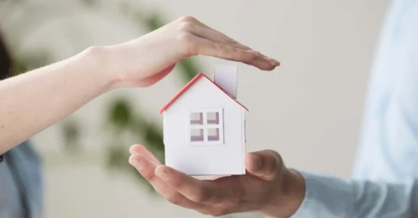 Une maison miniature protégée par des mains symbolisant la sécurité et la couverture d'une assurance emprunteur