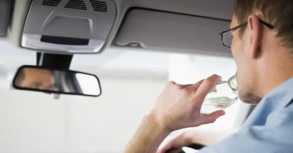 Un conducteur consommant de l'alcool au volant, illustrant les risques liés à l'alcoolémie et ses conséquences sur la sécurité routière et les assurances